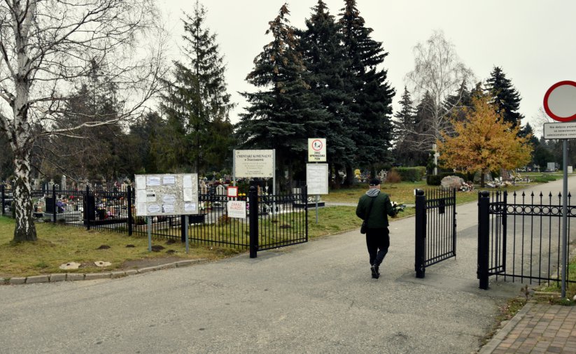 Mężczyzna z wiązanką kwiatów wchodzący na teren cmentarza 