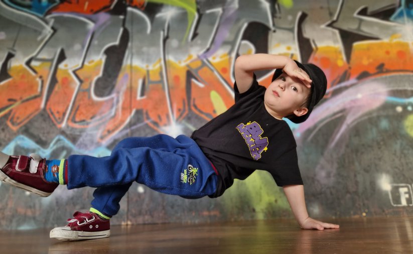 Młody chłopak tańczący breakdance, z tyłu graffitti
