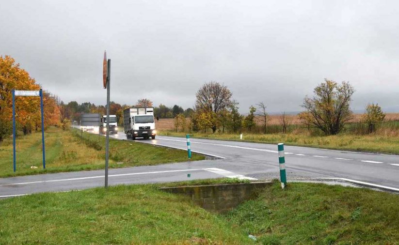 Dwa ciężarowe auta jadęce drogą, dookoła pola i kilka drzew