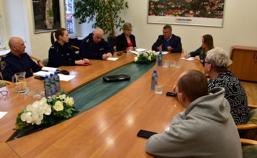 Strażnik miejski, policjanci oraz kobiety i mężczyźni po cywilnemu siedzący przy dużym owalnym stole