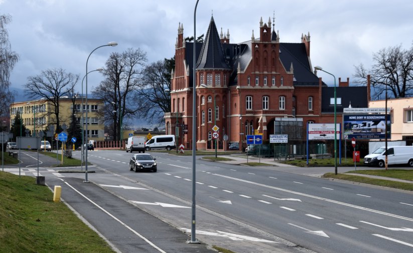 Szeroka droga, obok duża kamienica z czerwonej cegły