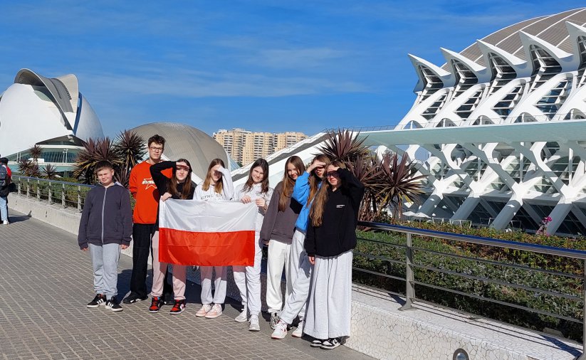 Osmioro uczniów na wspólnym zdjęciu, z przodu flaga Polski, bniebieskie niebo