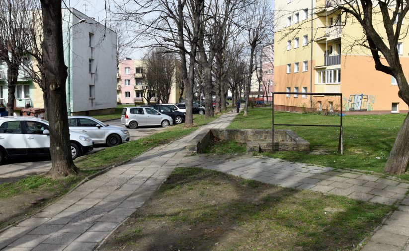 Osiedle, chodnik, obok zaparkowane auta,. w drugim planie bloki mieszkalne