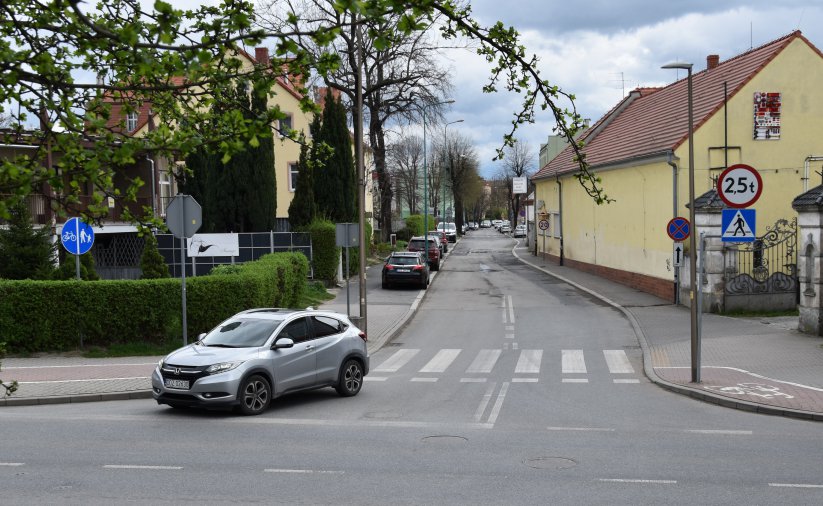 Skrzyżownie dróg, samochód włączający się do ruchu, po bokach zieleń i budynki