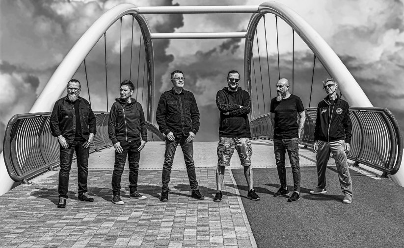 Sześciu mężczyzn stojąych w rzędzie, za nimi most, czarno-białe