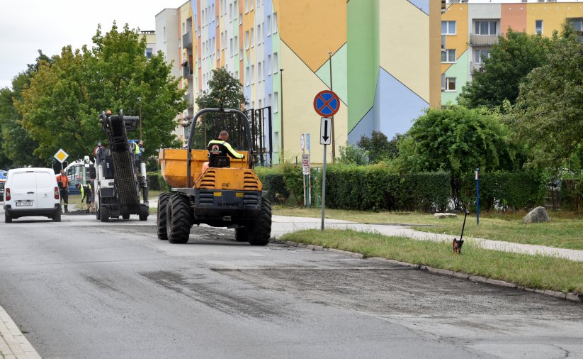 Droga osiedlowa, na części jezdni maszyny do prac drogowych w tle kolorowy blok