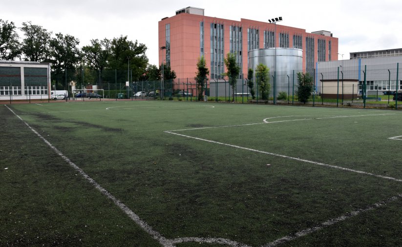 Boisko piłkarskie ze sztuczną trawą, za boiskiem duży czerwony budnek