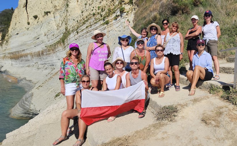 Grupa kobiet na kamenistej plaży, jedna z pań trzyma flagę Polski