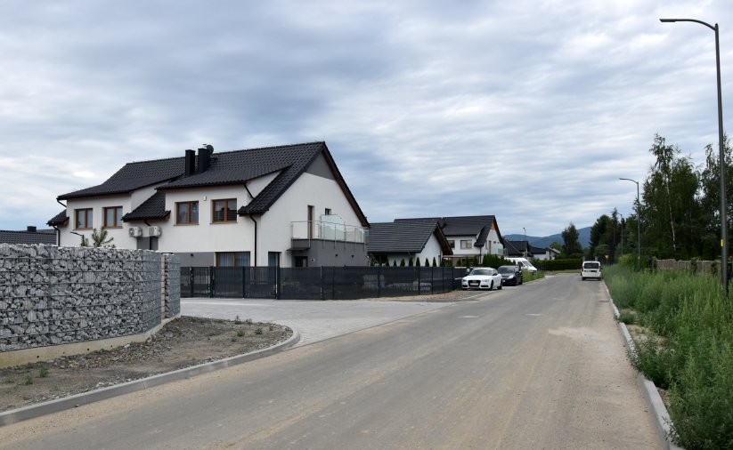 Ulica na osiedlu domków jednorodzinnych, Duży, biały dom, obok kamienny mur