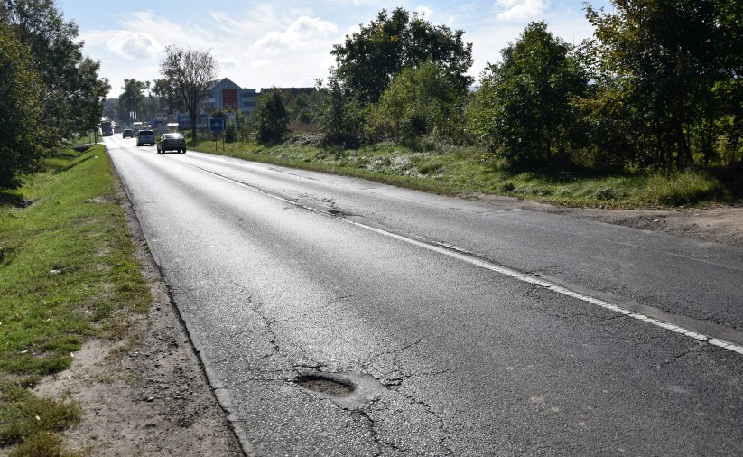 Droga asfaltowa prowadząca do miasta, w dali samochody, po bkach drzewa i krzewy