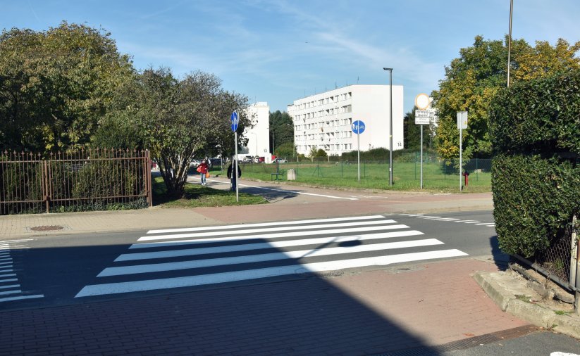 Przejście dla pieszych na drodze prowadącej na osiedle, w tle bloki mieszkalne