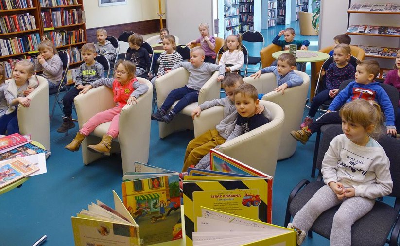 Przedszkolaki siedzące w fotelach w pomieszczeniu biblioteki, na pierwszym planie książki