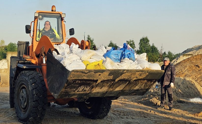 Worki z piaskiem na "łyżce" dużej koparki, obok hałdy piasku