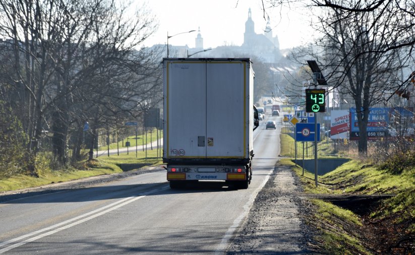 Ciężarówka jadąca drogą wjazdową do Dzierżoniowa, na poboczu tablica informująca kierowców o prędkości