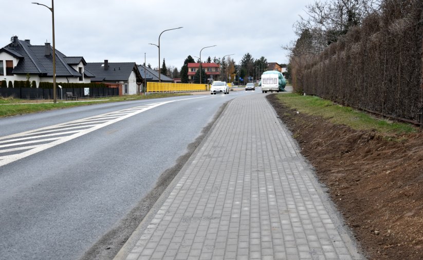 Droga i chodnik z kostki betonowej, po prawej stronie żywopłot, po lewej dom jednorodzinny