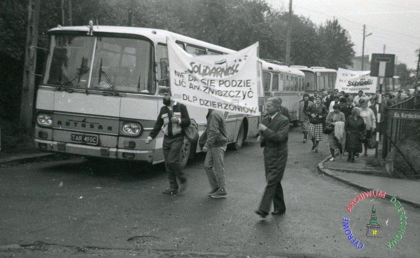 Archwialne zdjęcie ze stanu wojennego, ludzie idący w kolumnie, niosący napisy Solidarność, w tle kolumna autobusów