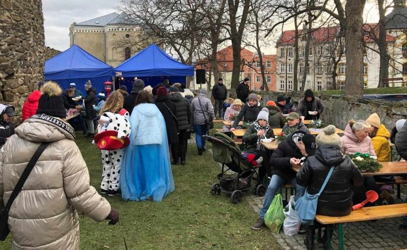 Ludzie siedzący przy stołach, po bokach kamienne, zabytkowe mury obronne