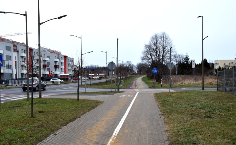 Szeroka ścieżka rowerowa przy drodze wyjazdowej z miasta, po lewej bloki mieszkalne