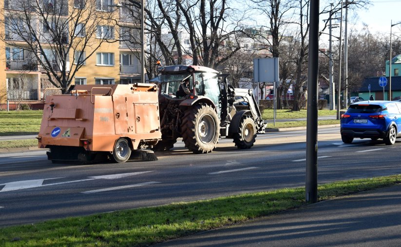 Maszyna zamiataqjąca drogę w mieście podczas ruchu samochodów