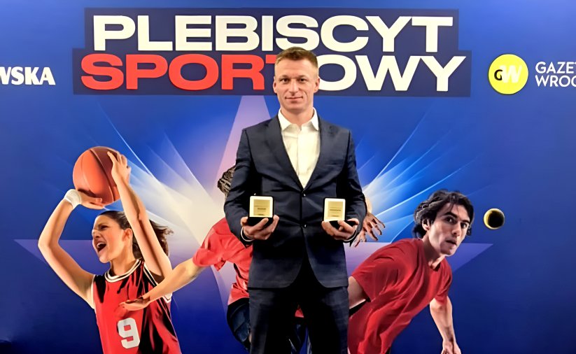 Patryk Ciszewski ze statuetkami w dłoniach, za nim napis Plebiscyt Sportowy