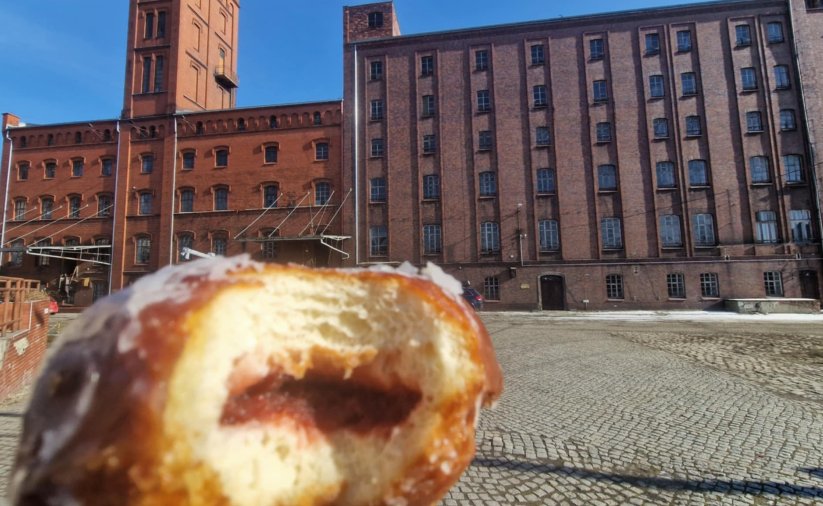 Nagryziony pączek, w tle budynek Młyna Hilberta z czerwonej cegły