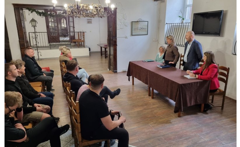 Grupa osób siedzi na krzesłach podczas spotkania.
