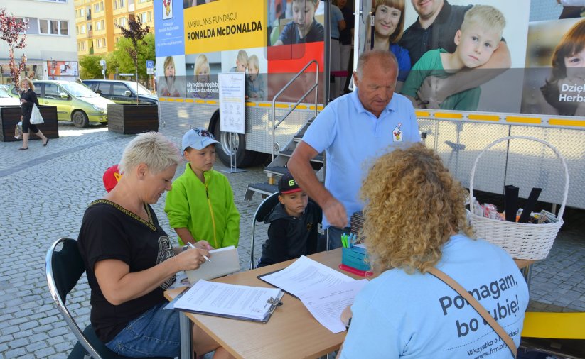 Rejestracja przed ambulansem fundacji Ronalda McDonalda w dzierżoniowskim Rynku, Kobieta i mężczyzna z dziećmi są przyjmowani w rejestracji