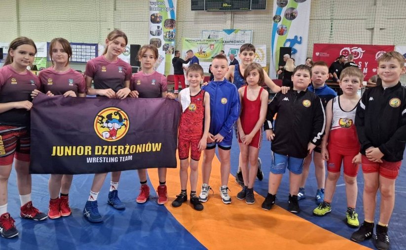 Grupowe zdjęćie kilkunastu młodych zapaśniczek i zapaśników w hali sportowej