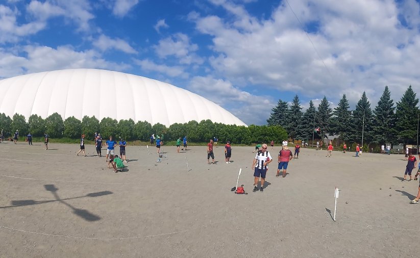 Duży plac, ludzie grający grupkami w petanque