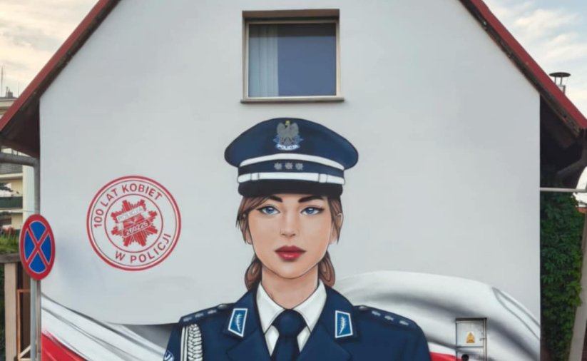 Malowidło na fasadzie budynku, przedstawiające kobietę policjantkę w mundurze, w tle polska flaga i napis 100 lat kobiet w policji