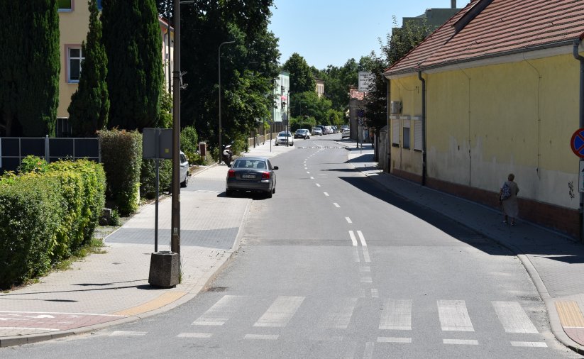 Ulica Słowiańska, na pierwszym planie przejście dla pieszych, na chodniku po lewej zaparkowane auta, obok zieleń