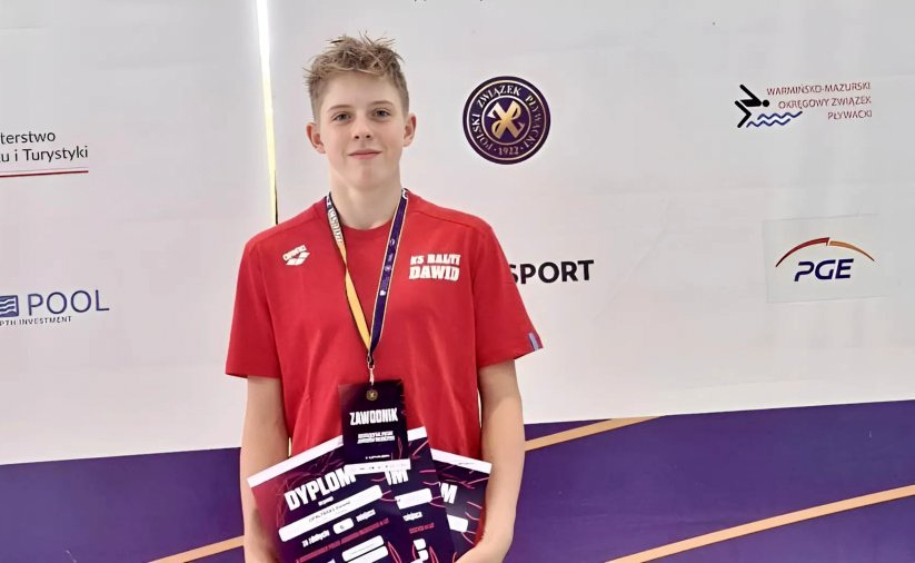 Dawid Opaliński w czerwonej koszulce z medalem na szyi i z dyplomami w rękach