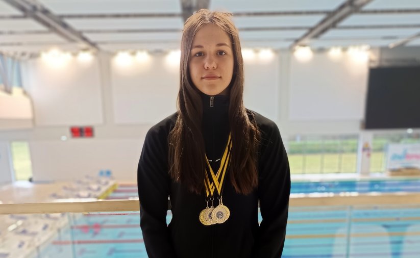 Natasza Paraciej z medalami na szyi przy niecce basenu krytego