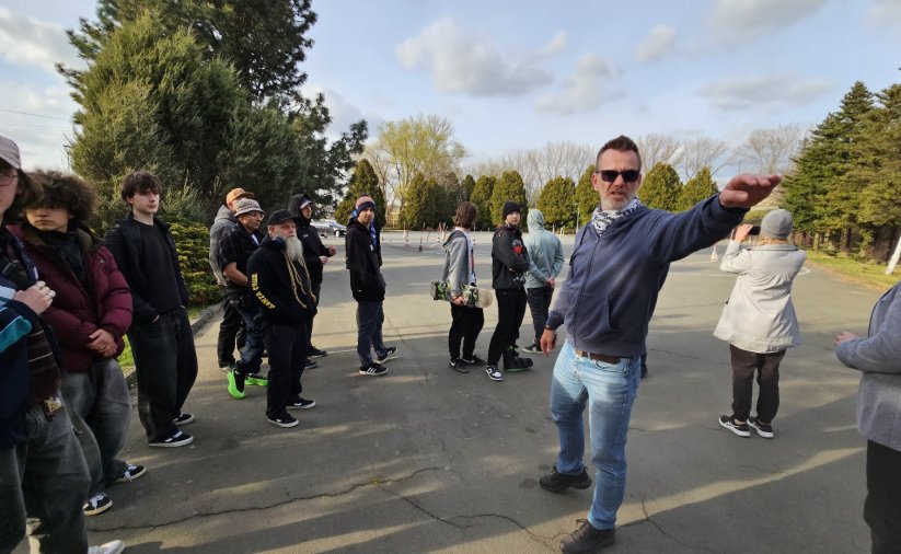Grupa mężczyzn na placu manewrowym, jeden z nich coś pokazuje ręką
