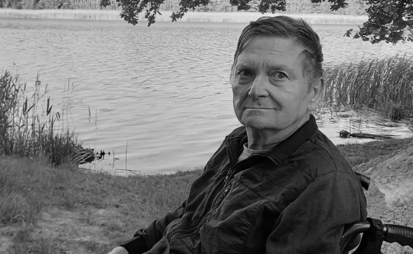 Czarno-białe zdjęcie mężczyzny na wózku inwalidzkim, w tle zbiornik wodny