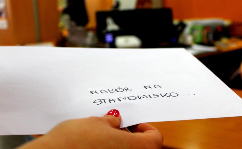 Ręka z kopertą z napisem "Nabór na stanowisko" na tle Biura Obsługi Klienta