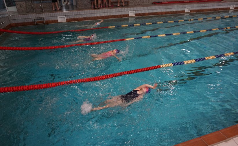 dzieci pływające na basenie grzbietem