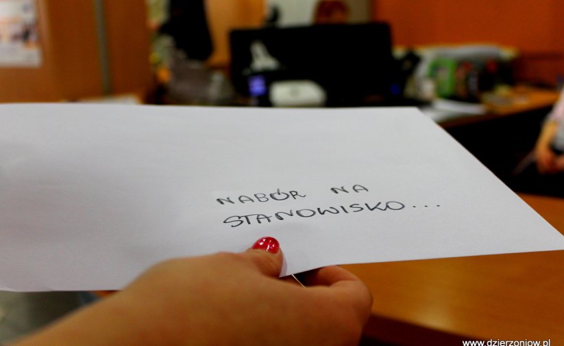 Zdjęcie ręki trzymającej kopertę z napisem "Nabór na stanowisku..." na tle Biura Obsługi Klienta