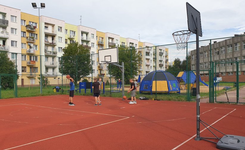 Czwórka chłopców na boisku do kosza, za nimi długi blok