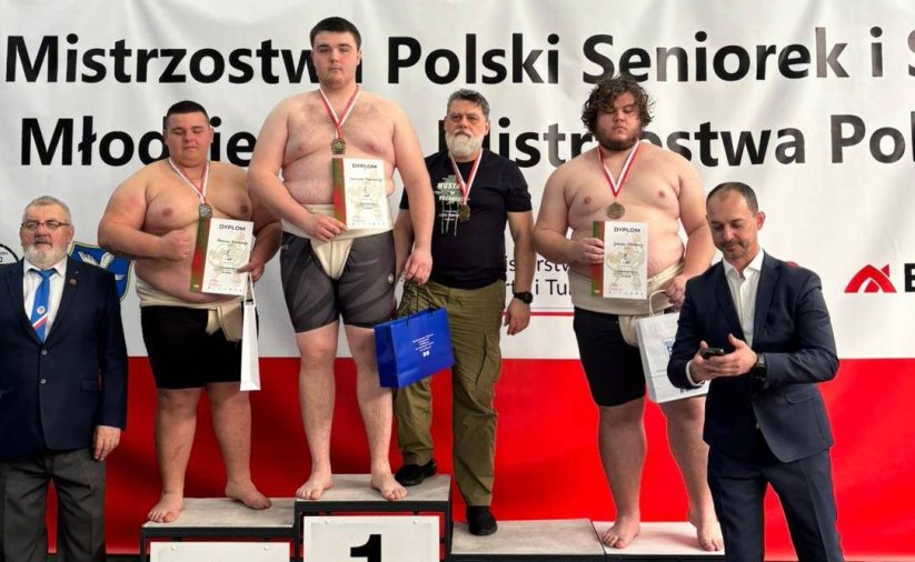Zawodnicy sumo stojący na podium na biało-czerwonym tle