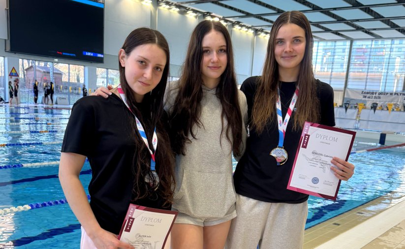Trzy pływaczki, w tym dwie z dyplomami, na tle basenu