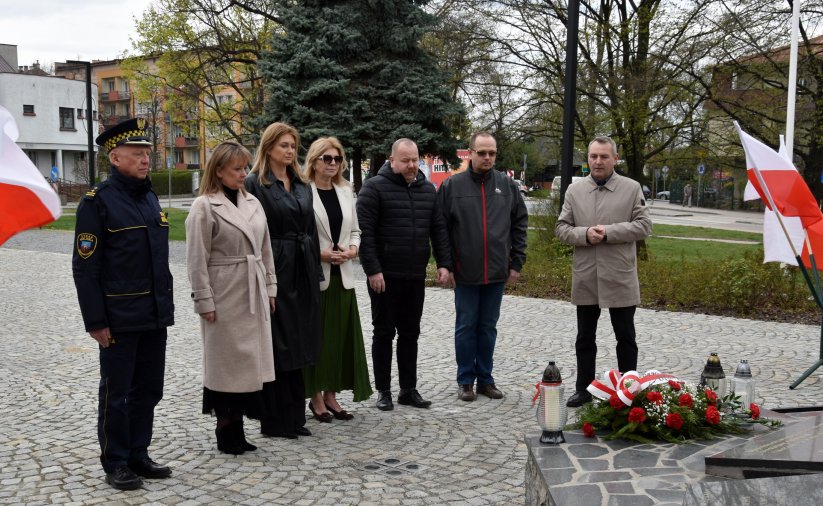 Trzy kobiety i czwórka mężczyzn stoją przed pomnikiem, po bokach flagi Polski