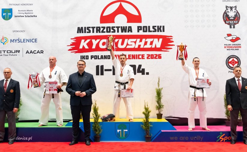 Trzech karateków na podium, Tomasz Staściuk na pierwszym miejscu z uniesionym w górę pucharem 
