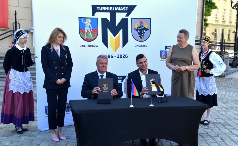 Burmistrz Dzierżoniowa i Chojnic siedzą przy stole, trzymają pospisane umowy