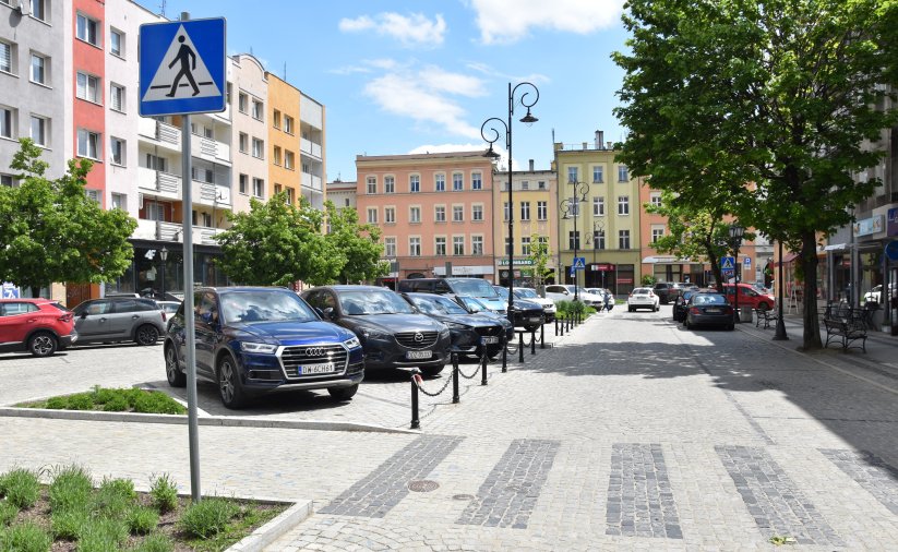 Rynek, zaparkowane samochody, w tle budynki, na pierwszym planie przejście dla pieszych