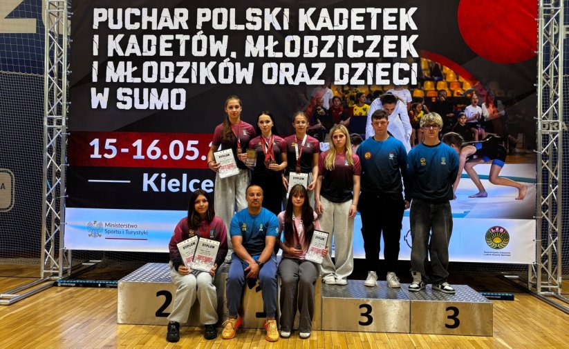 Sześć dziewczyn i dwóch chłopaków w jednakowych strojach stoją i siedzą z trenerem na podium