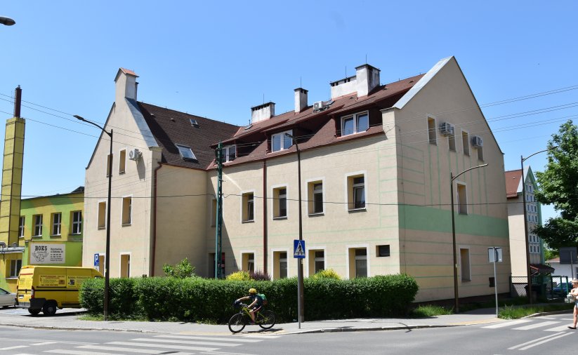 Trzypiętrowy budynek ze spadzistym dachem i piaskowym kolorem elewacji