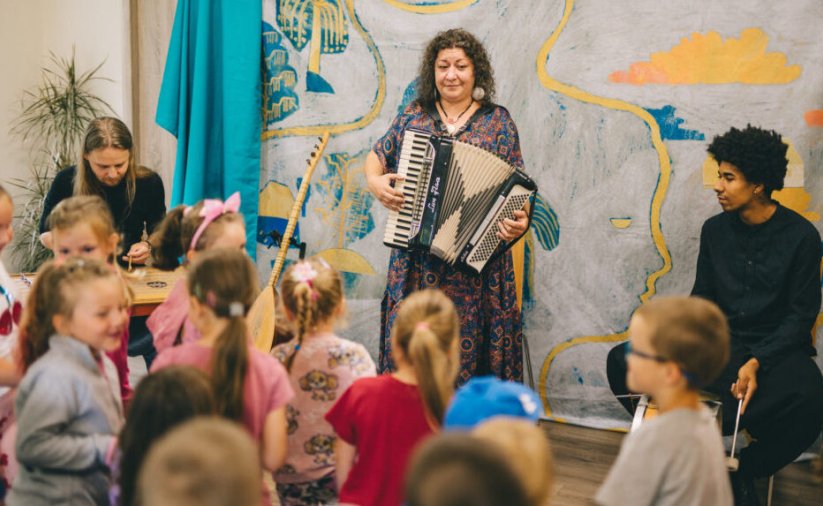 Kobieta grająca na harmonii, przed nią grupa dzieci