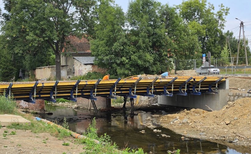 Most w budowie nad niewielką rzeką, w tle drzewa