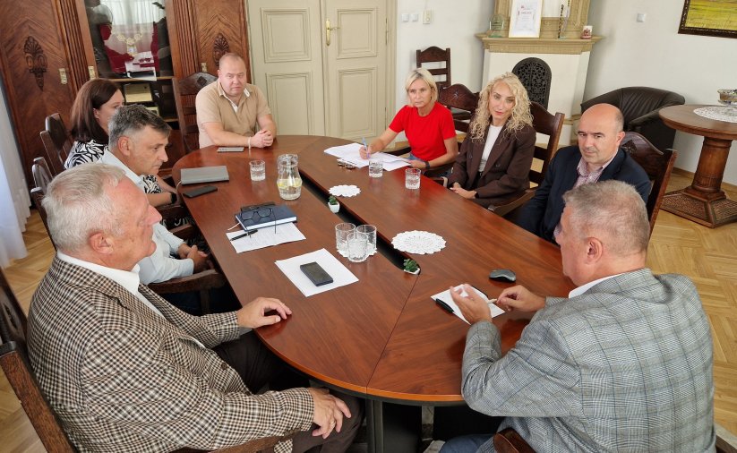 Ośmioro uczestników spotkania siedzących przy owalnym stole w gabinecie burmistrza